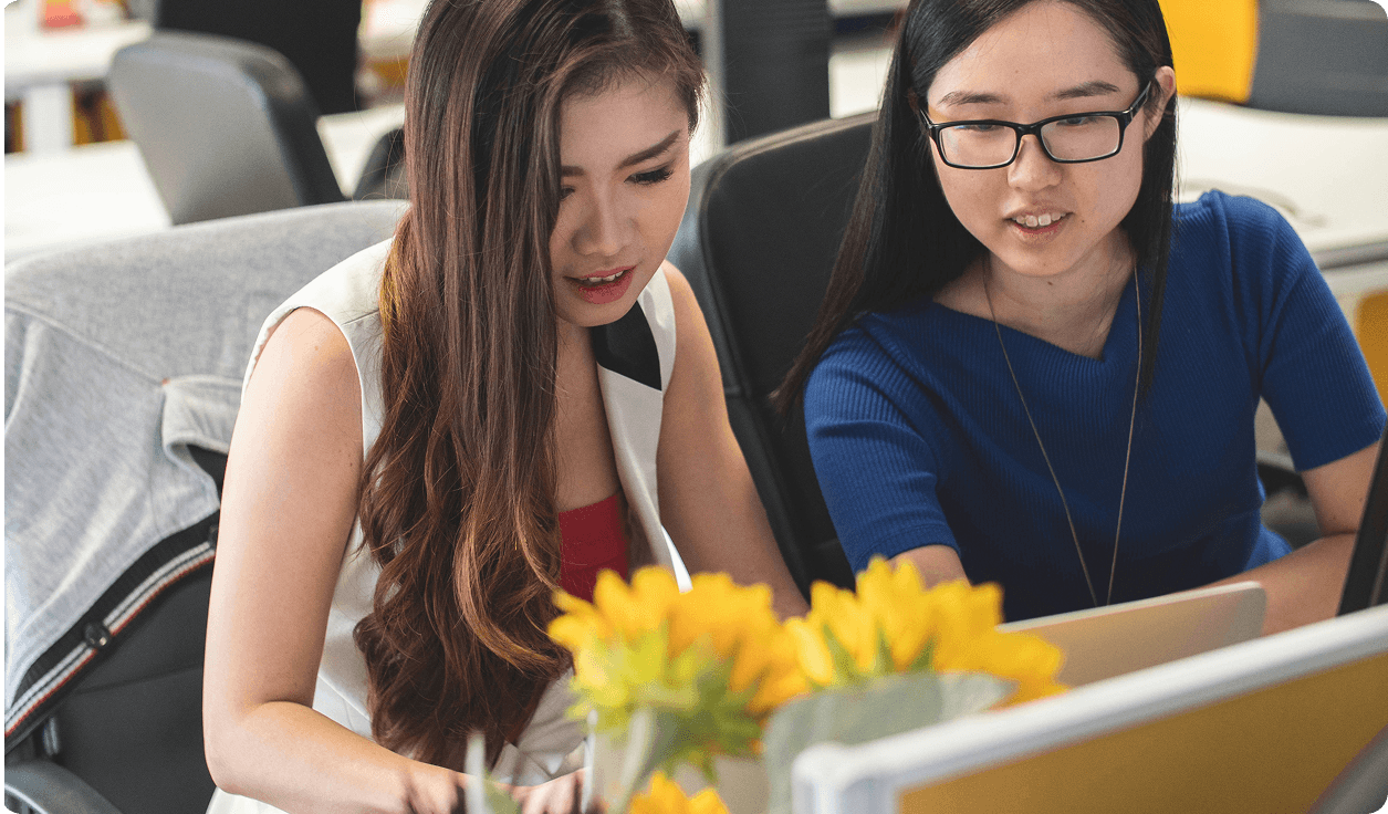 Two young women studying together at a desk with laptops